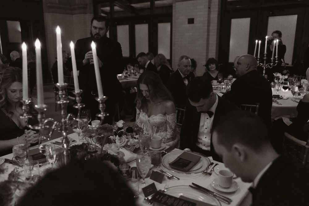 Formal dinner setting with white candles illuminating tables in a dark banquet hall.