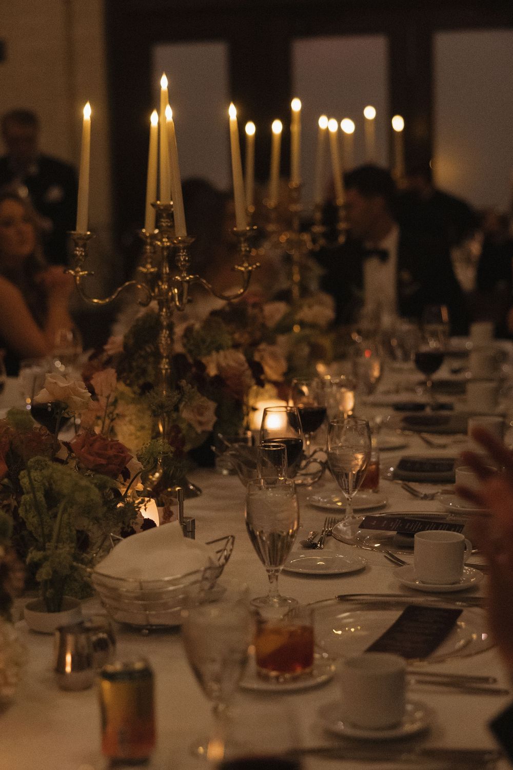 Elegant candlelit dining tables set with white linens, floral centerpieces and glowing tapered candles create a romantic atmosphere.