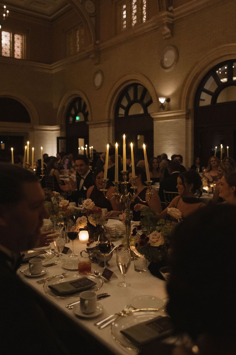 Elegant formal dining setup with candlelit tables and arched windows in a grand ballroom setting.