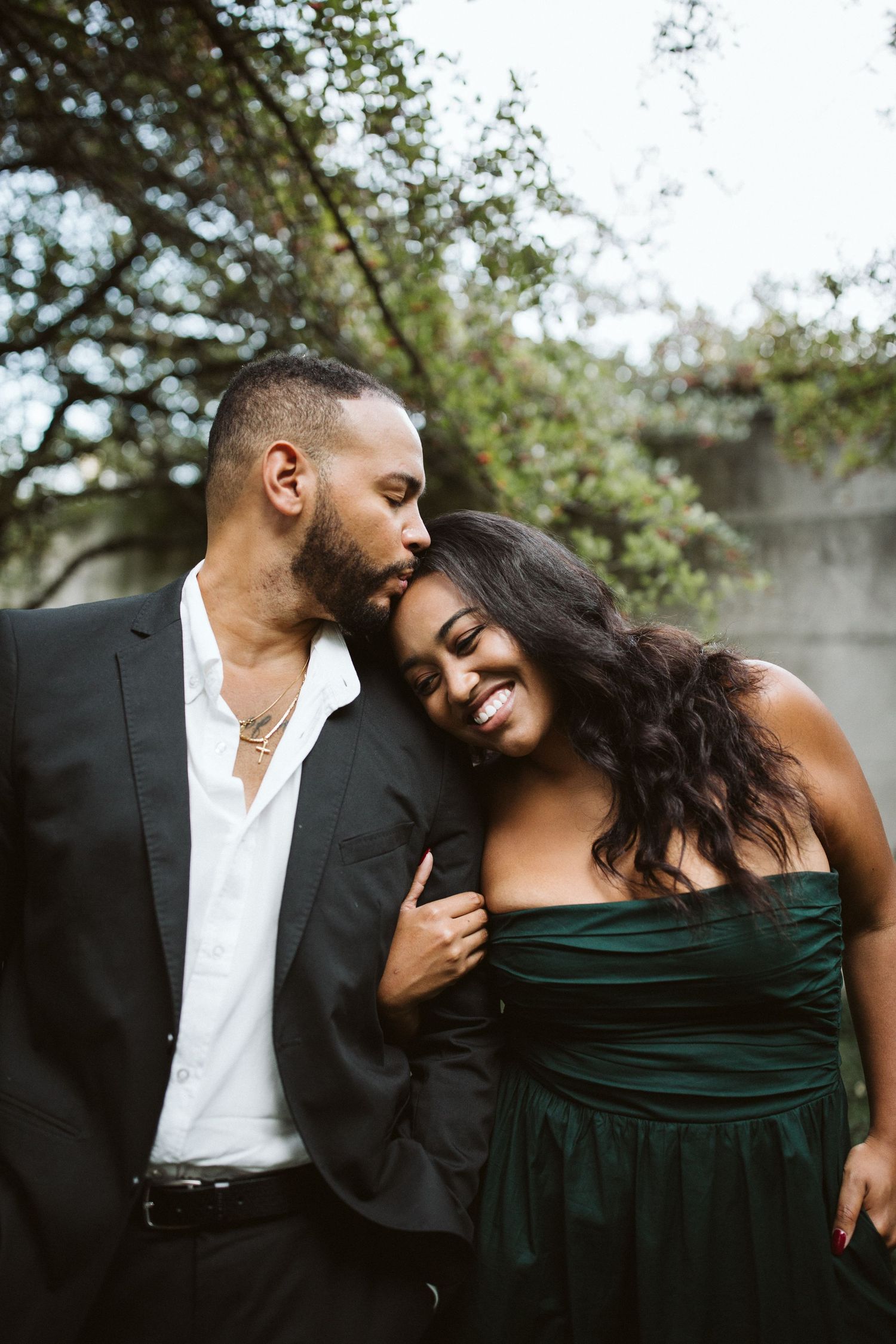 Romantic couple sharing intimate moments in a garden setting wearing formal black and green attire.