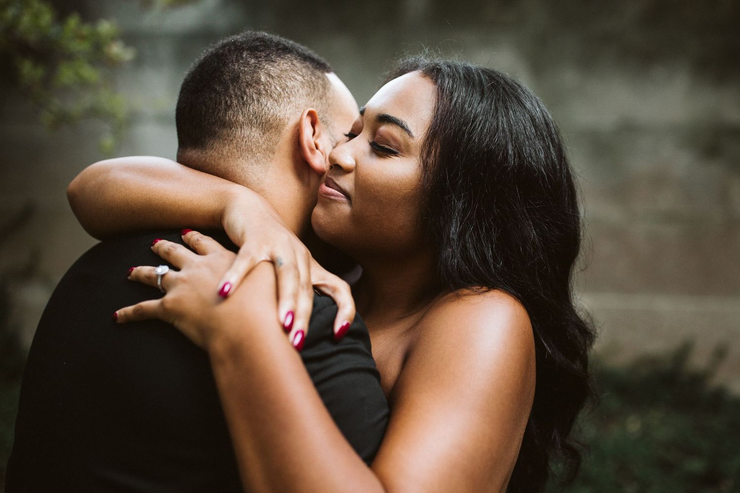 A romantic couple embraces in an intimate outdoor portrait showing an engagement ring.
