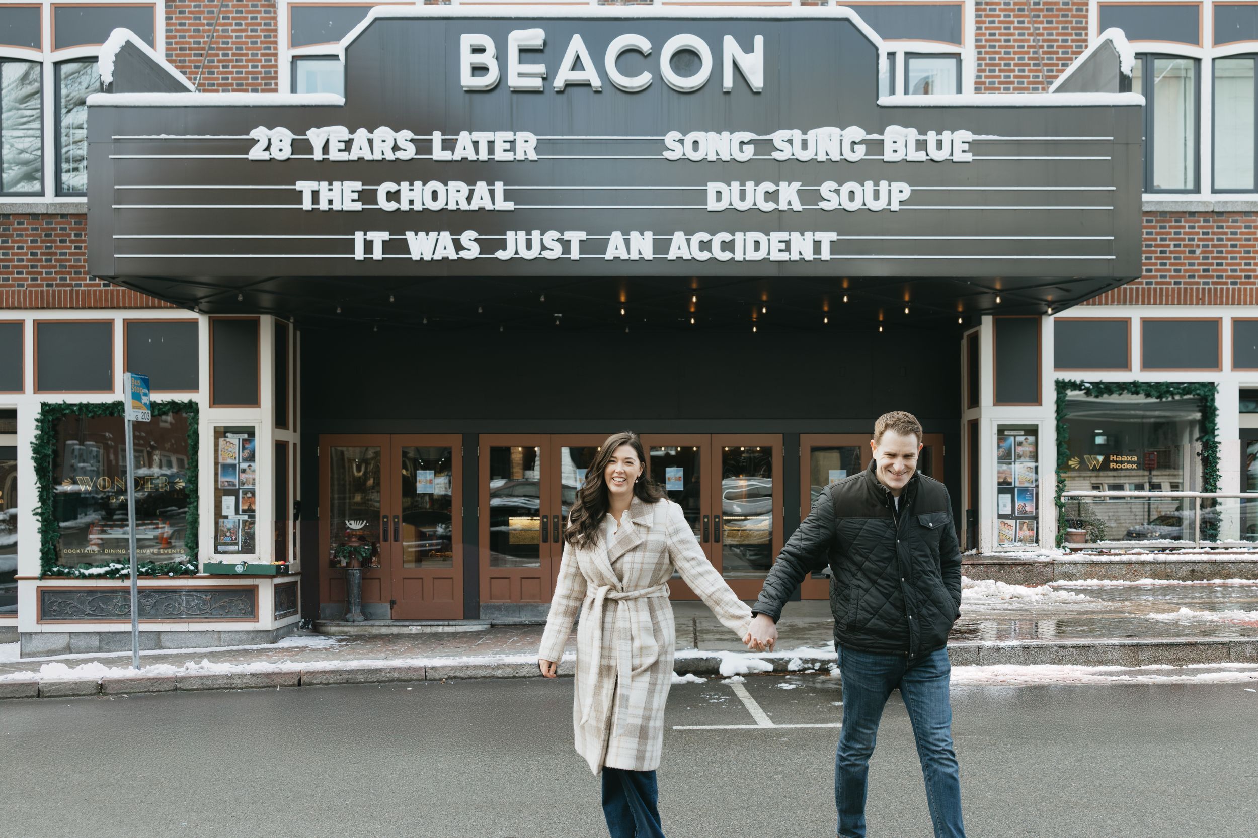 A vintage movie theater marquee shows 'Beacon' and other text against a brick building facade.