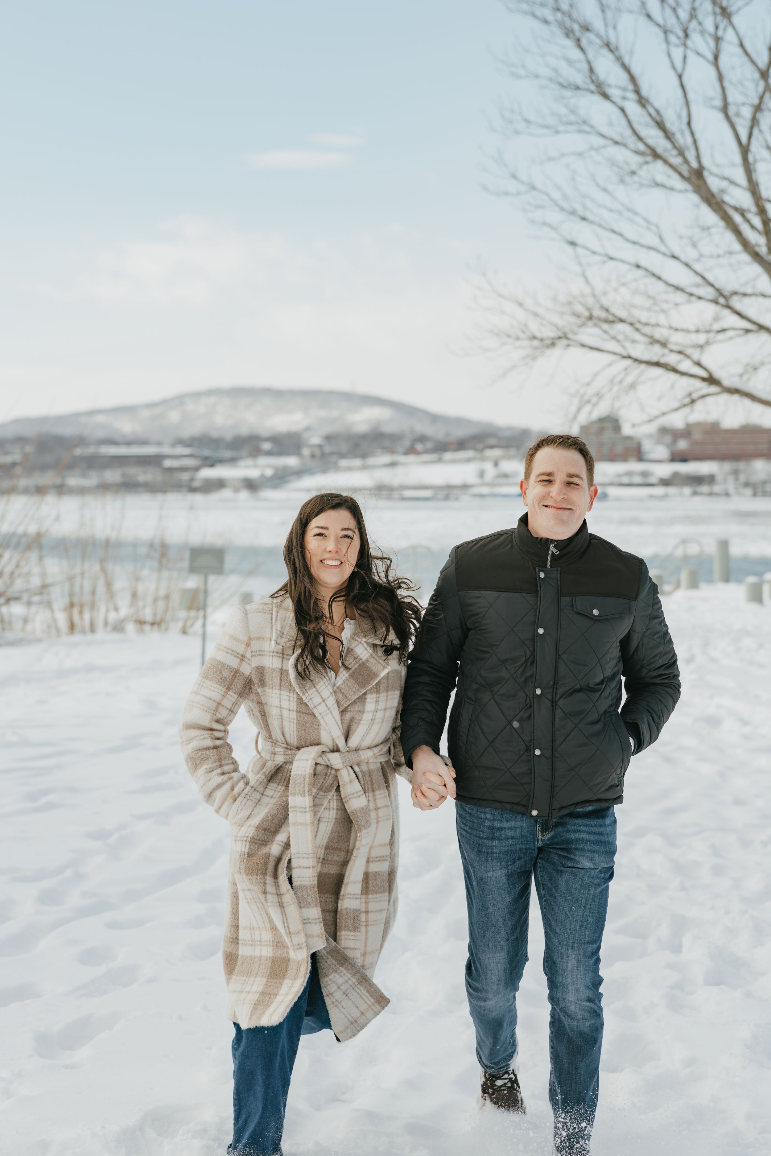 A couple shares joyful moments together in a snowy winter landscape with mountains visible in the background.