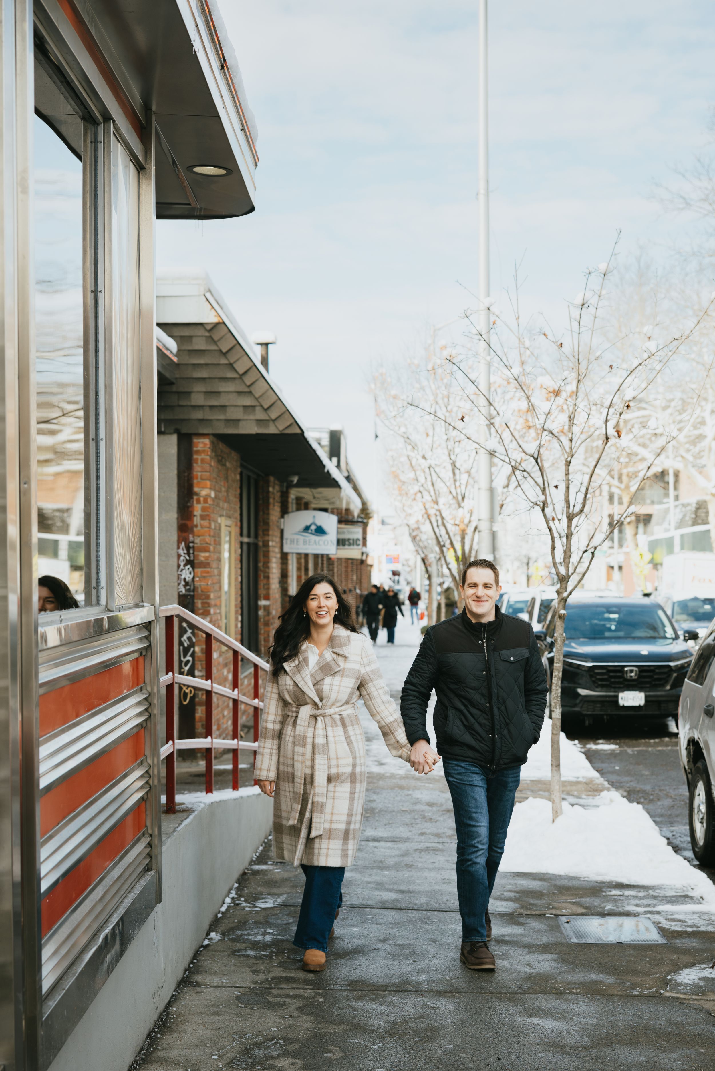 People walking along a snowy sidewalk outside a commercial building with large windows on a winter day.
