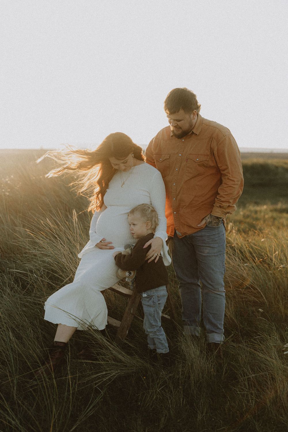 Family shares intimate moment together in field of tall grass at sunset.
