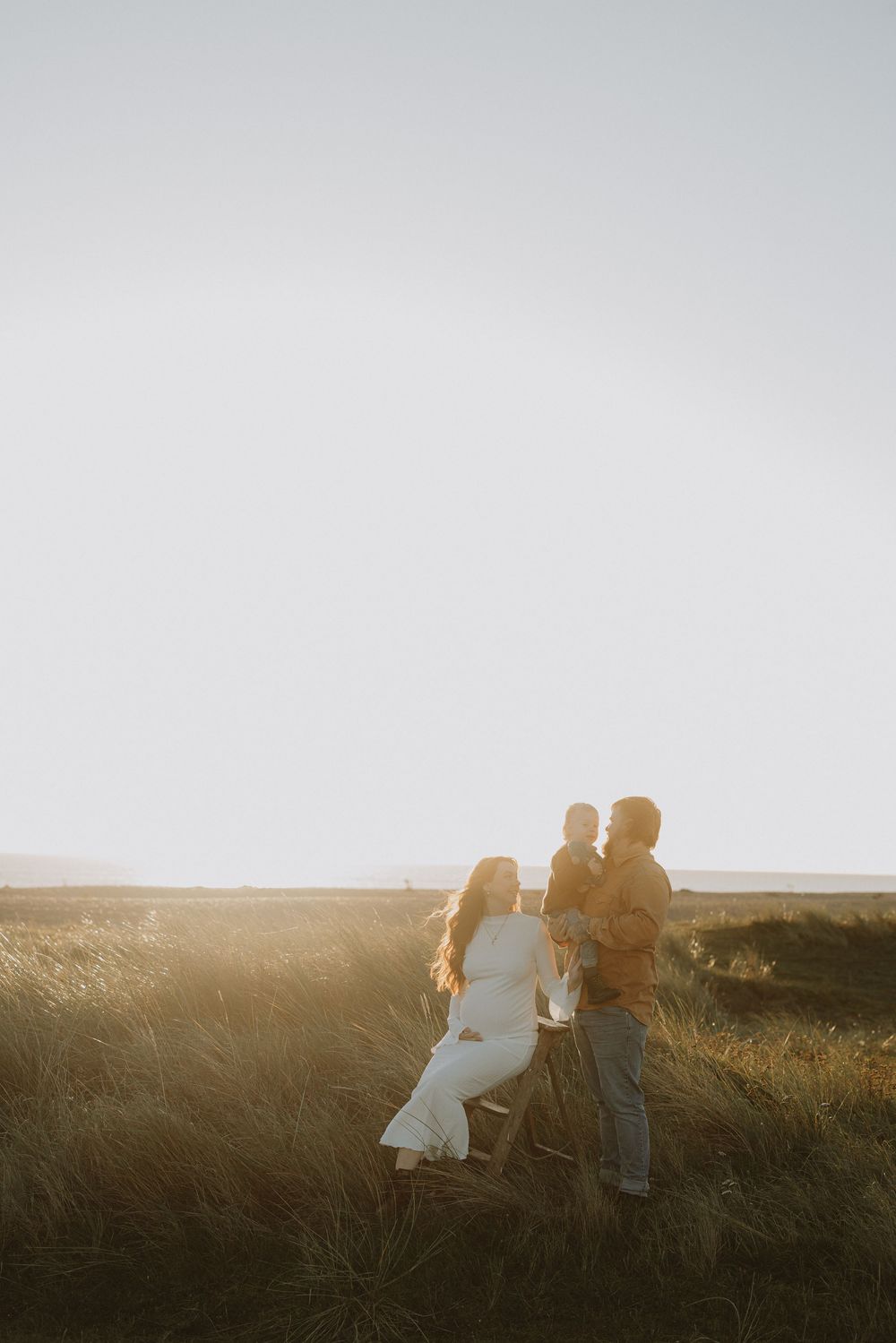 A couple walking together in a grassy field during golden hour sunset.