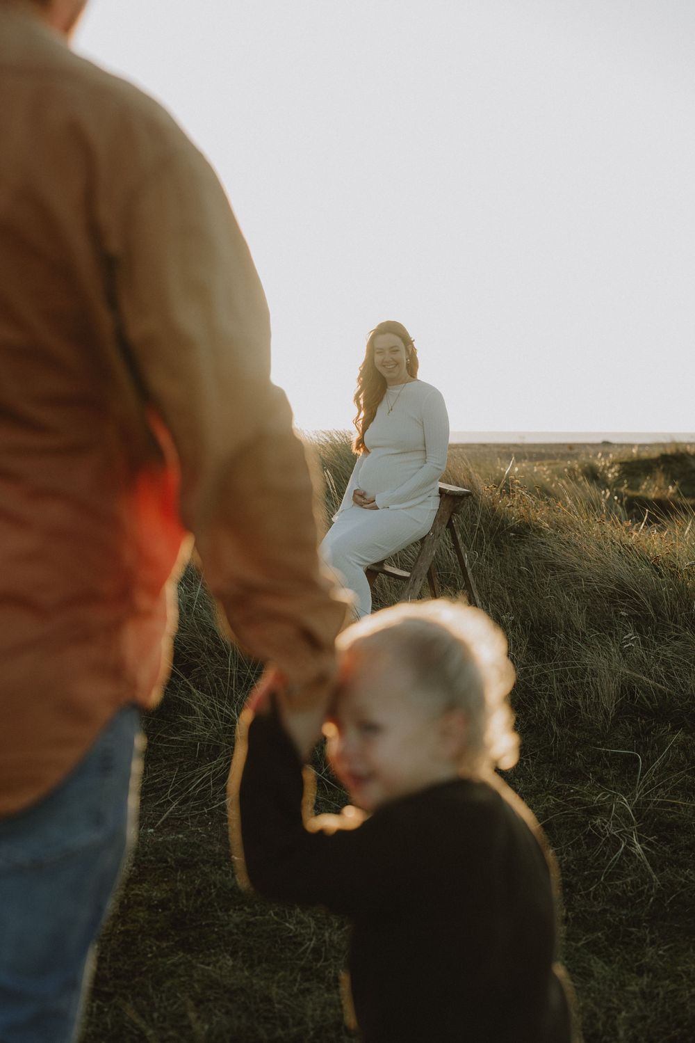 Family enjoying a playful moment together on a grassy hillside during sunset.
