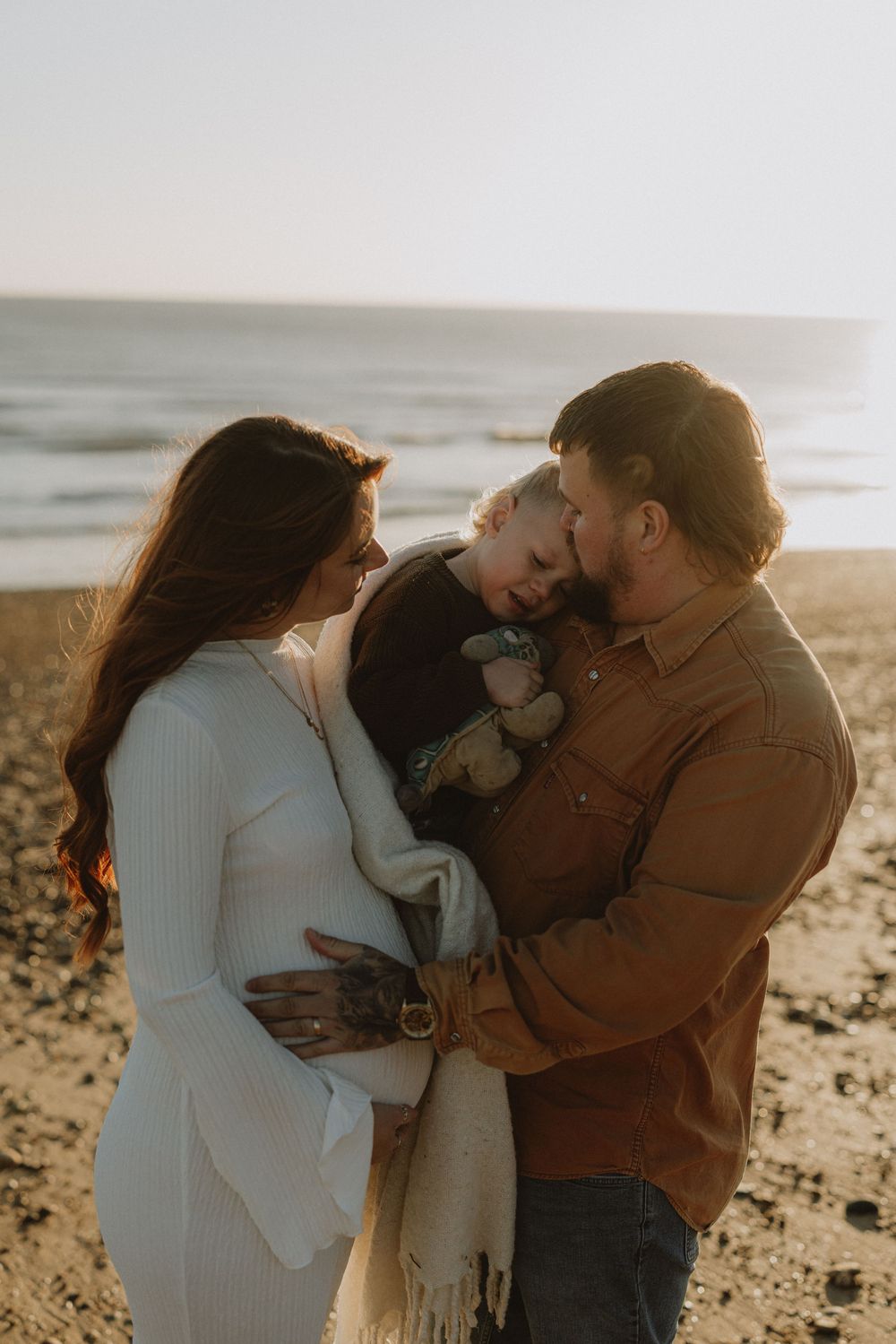Tender family moment captured on beach during golden hour sunset.