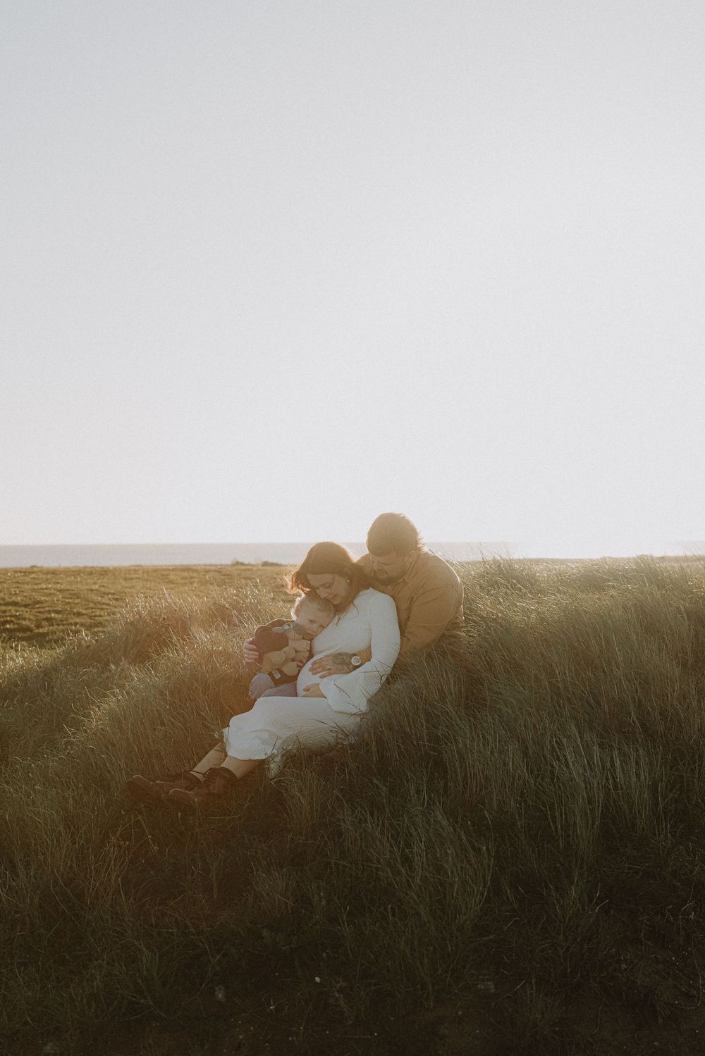Couple relaxing together in tall grass during golden hour with warm sunlight creating a dreamy atmosphere.