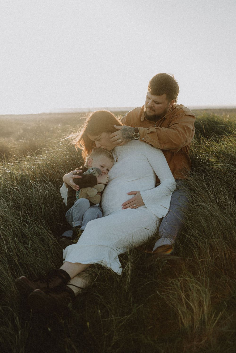A couple shares an intimate moment lying together in tall grass during golden hour sunset.