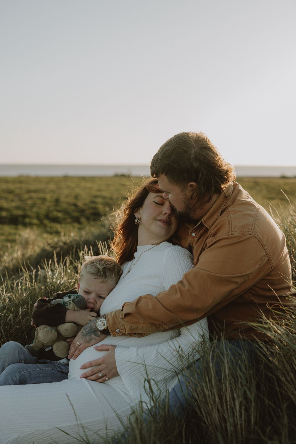 Family lying together on a blanket in a grassy meadow at sunset.