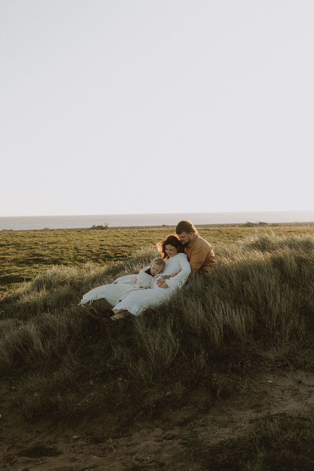 People relaxing in tall grass on a hill overlooking a vast natural landscape at sunset.