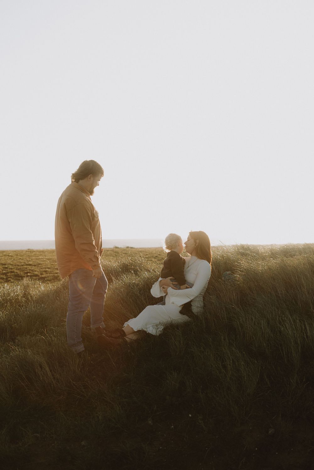 Silhouetted figures sit together on a grassy hillside at dusk.