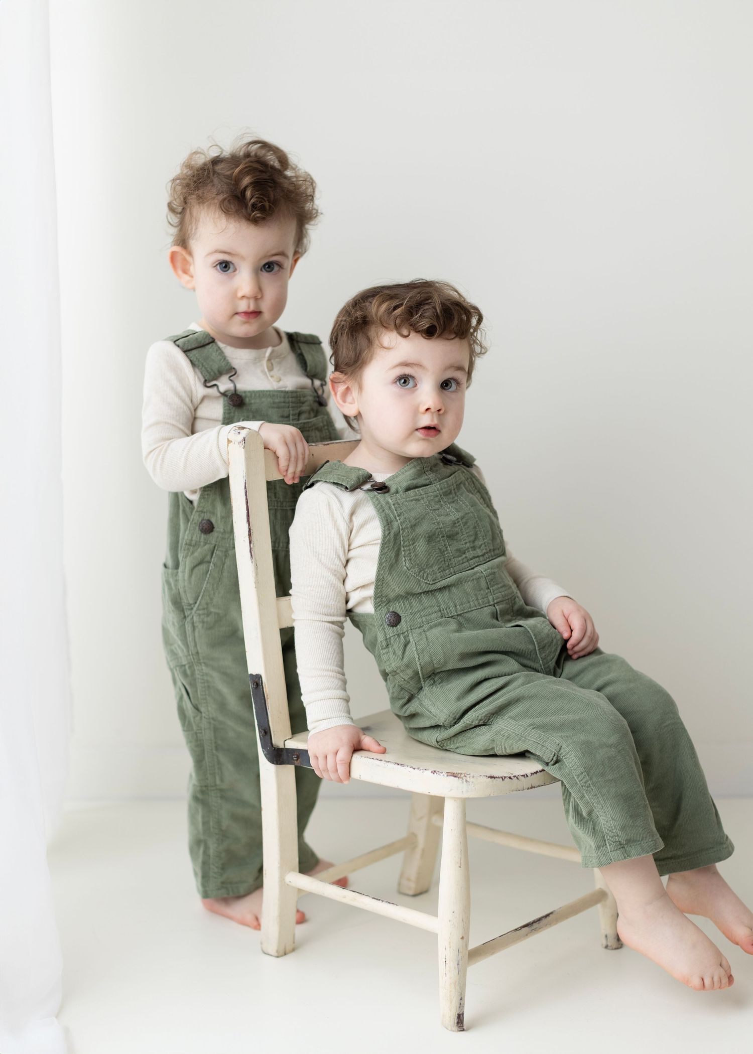 Three photos of toddlers in green overalls sitting on a rustic white wooden chair against a neutral background.
