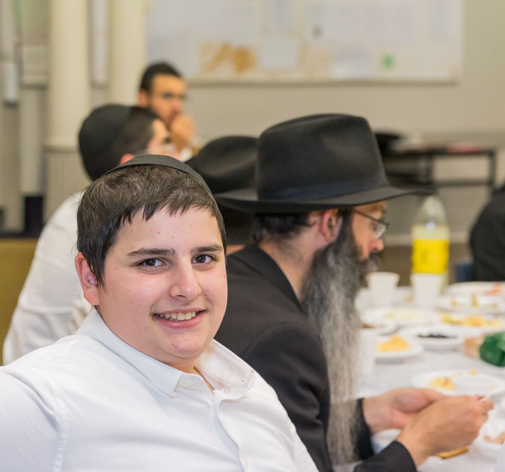 People gather around a table at what appears to be a Jewish gathering or celebration.