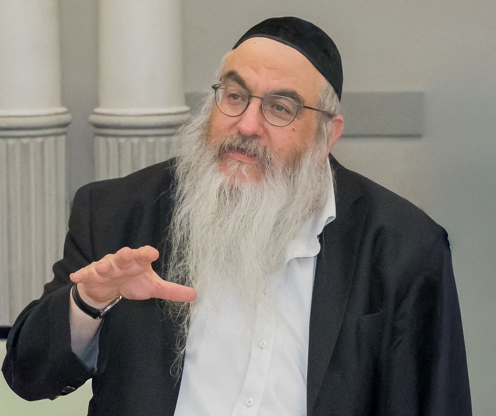 A person in a black suit and white beard makes various expressive gestures in a collage of four photos.