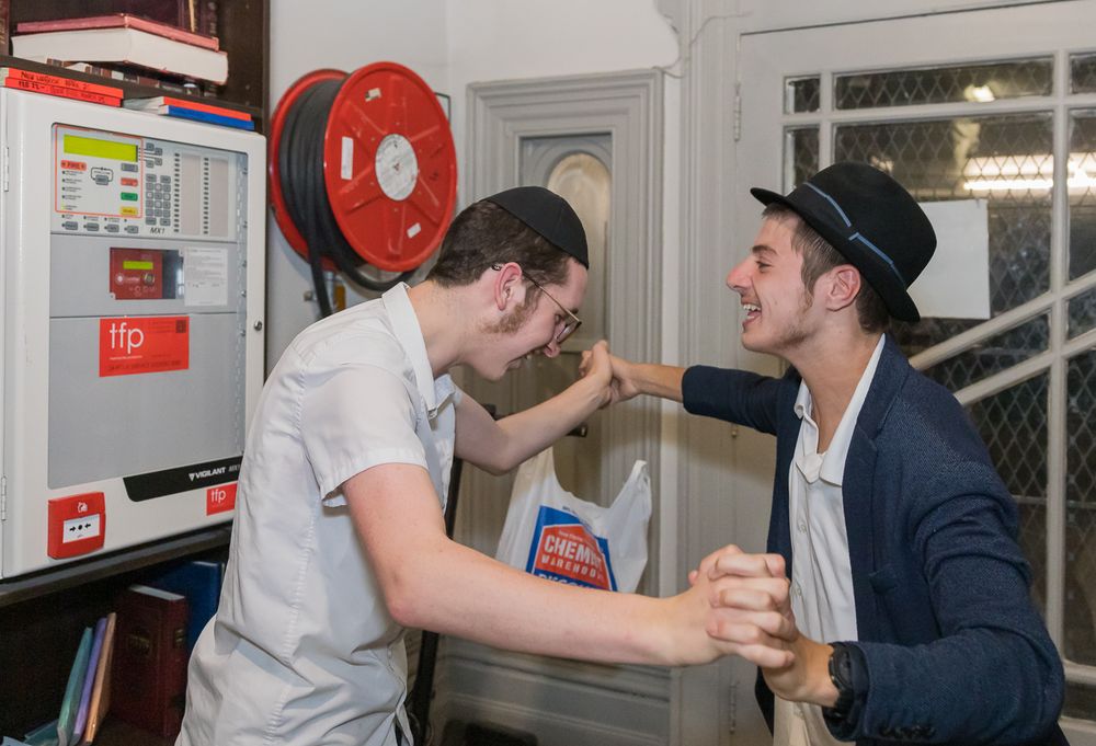 Two people laughing and playfully interacting in a casual indoor setting with a red fire safety device on the wall.