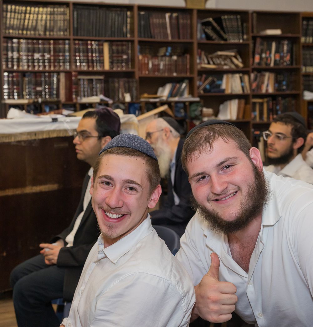 A group of students in white shirts smile and interact in what appears to be a library setting.