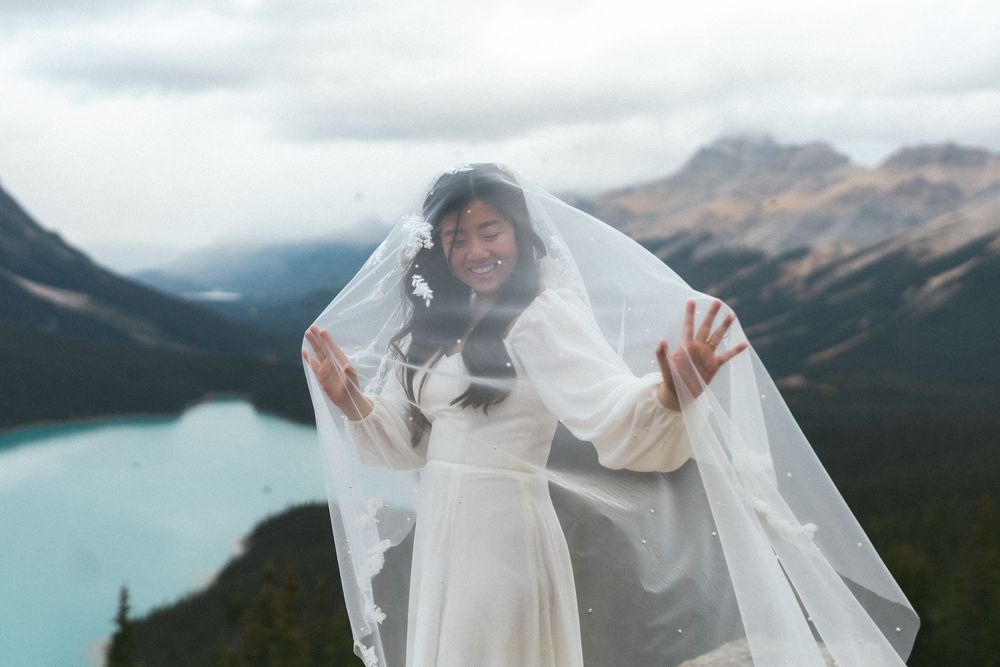 bride laughs as she moves her hands beneath her veil dramatically with mountains in the background
