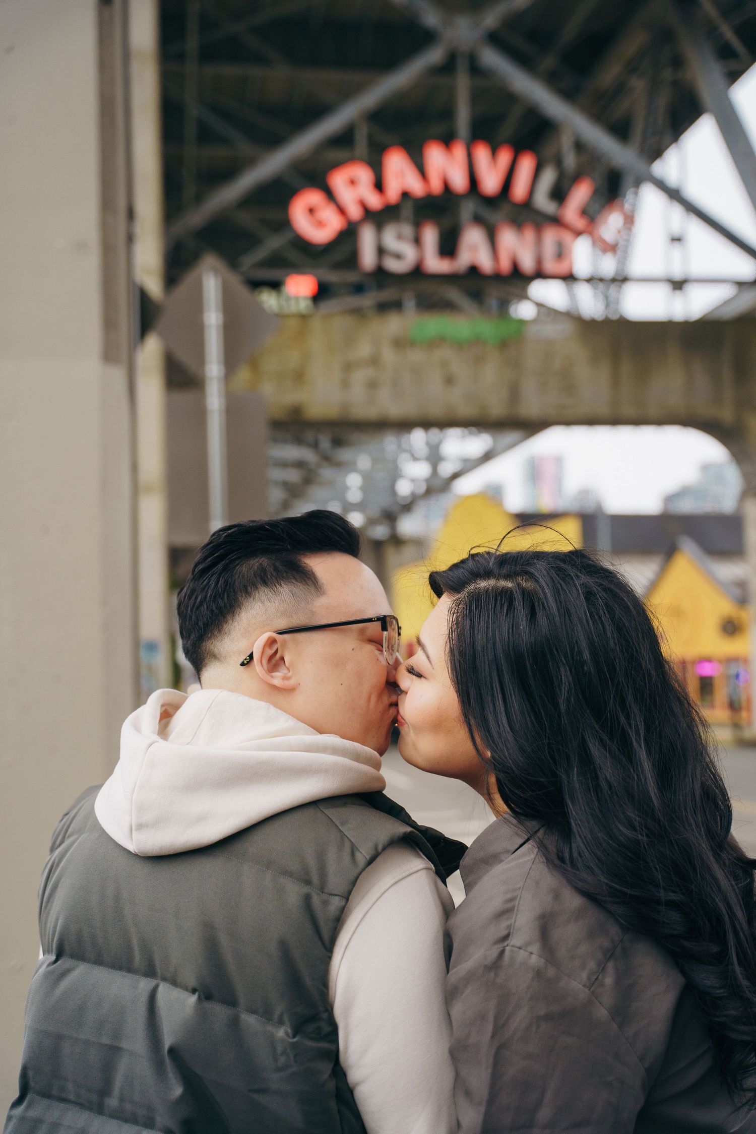 A couple shares a romantic kiss in front of the Granville Island sign in Vancouver.