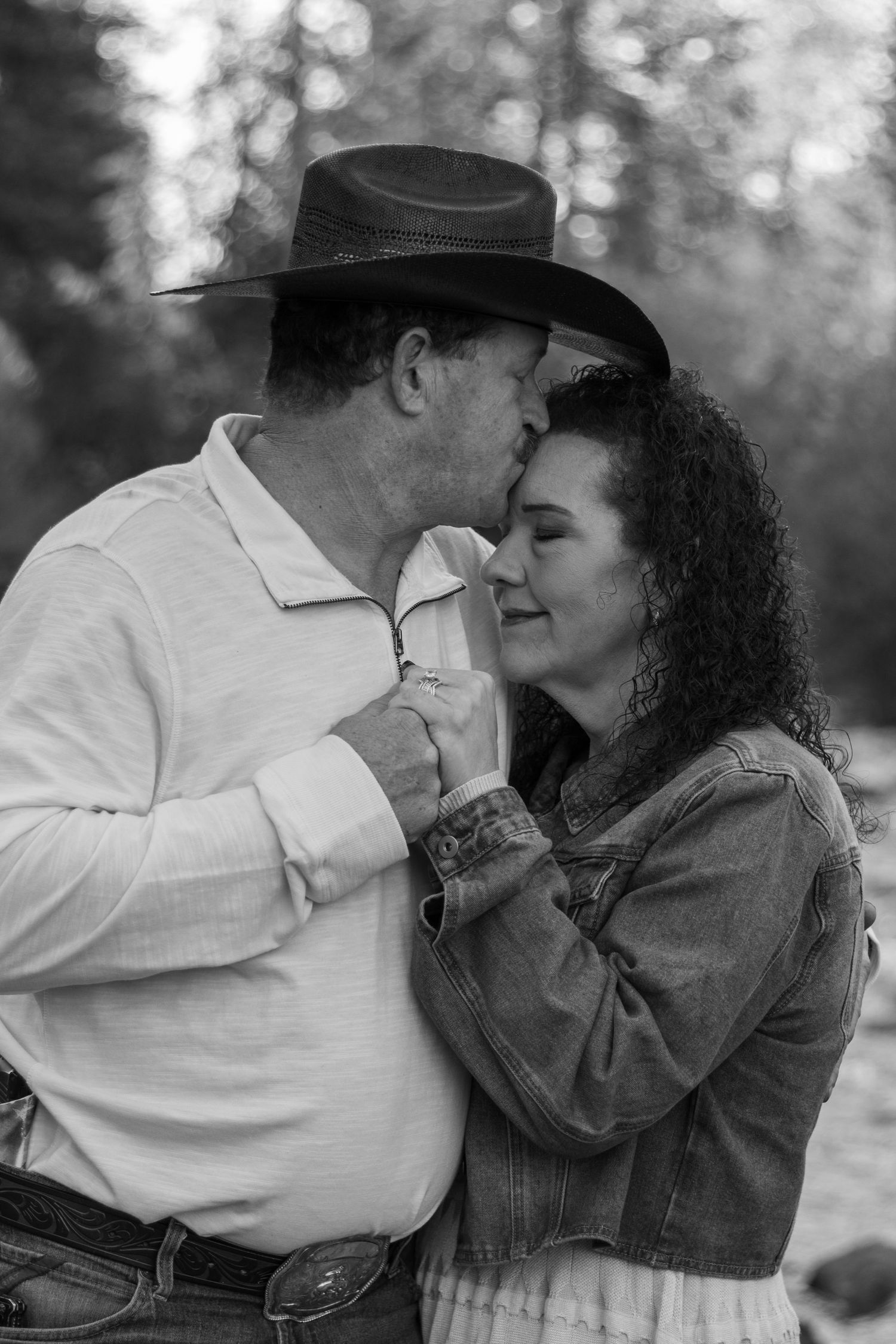 Black and white photo of man in cowboy hat kissing womans forehead tenderly.
