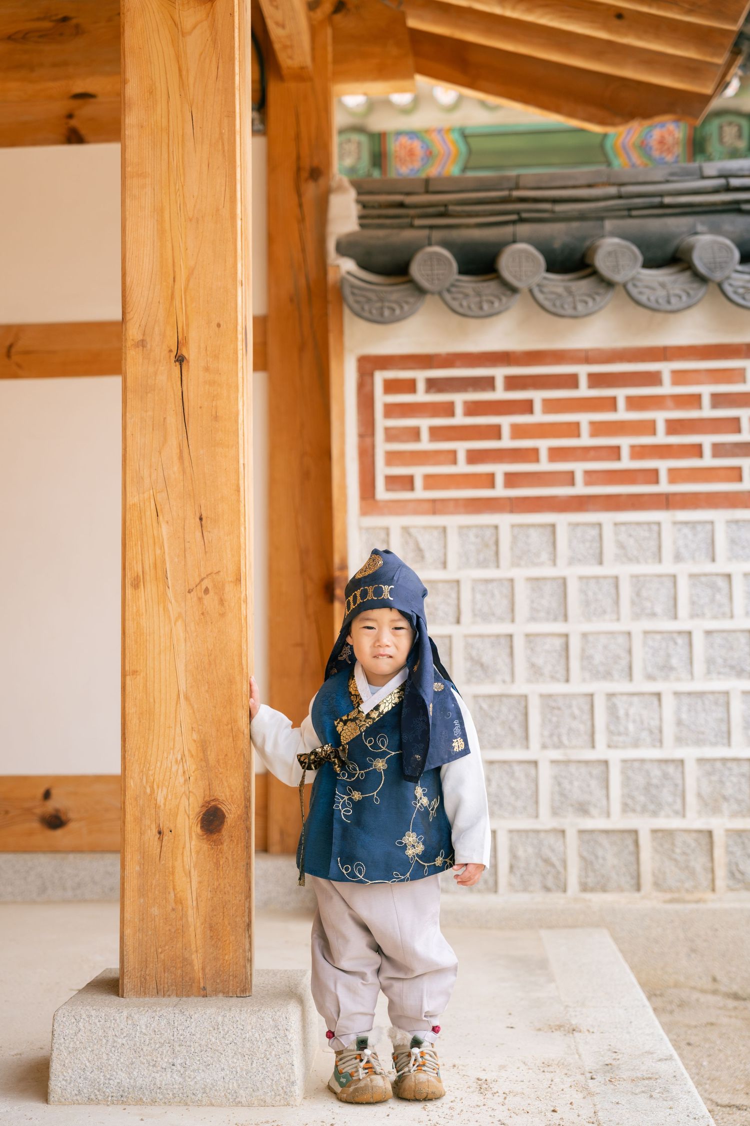 A small child stands in traditional Korean hanbok clothing at a temple with wooden pillars and ornate roof tiles.