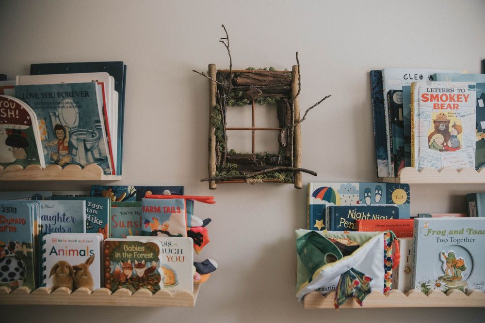 A collection of children's books and decorative items displayed on white floating shelves against a wall.