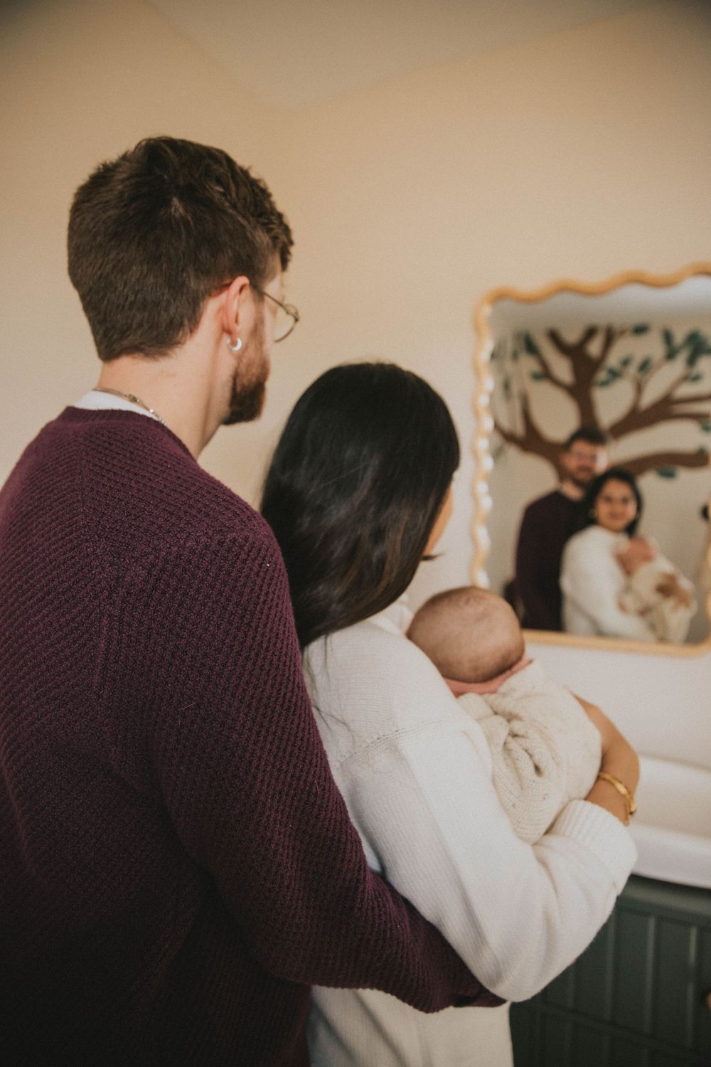 A couple in burgundy and white clothing share an intimate embrace in a softly lit indoor setting.