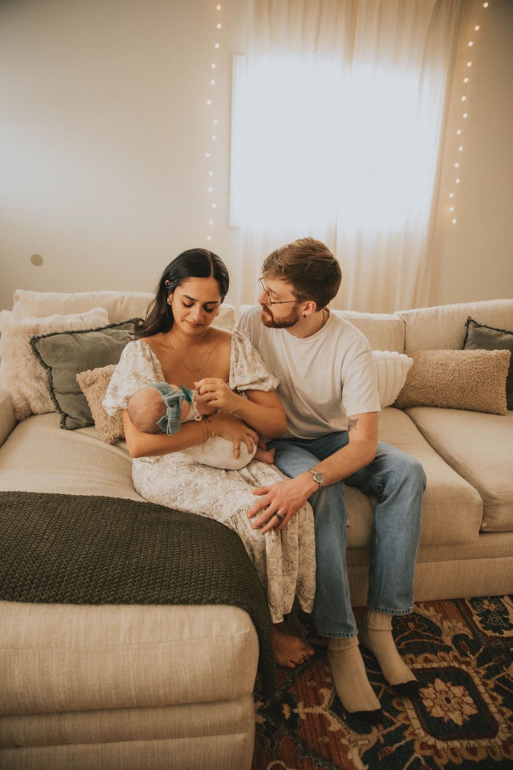 Couple relaxing together on a beige couch in a cozy living room with warm lighting and patterned rug.