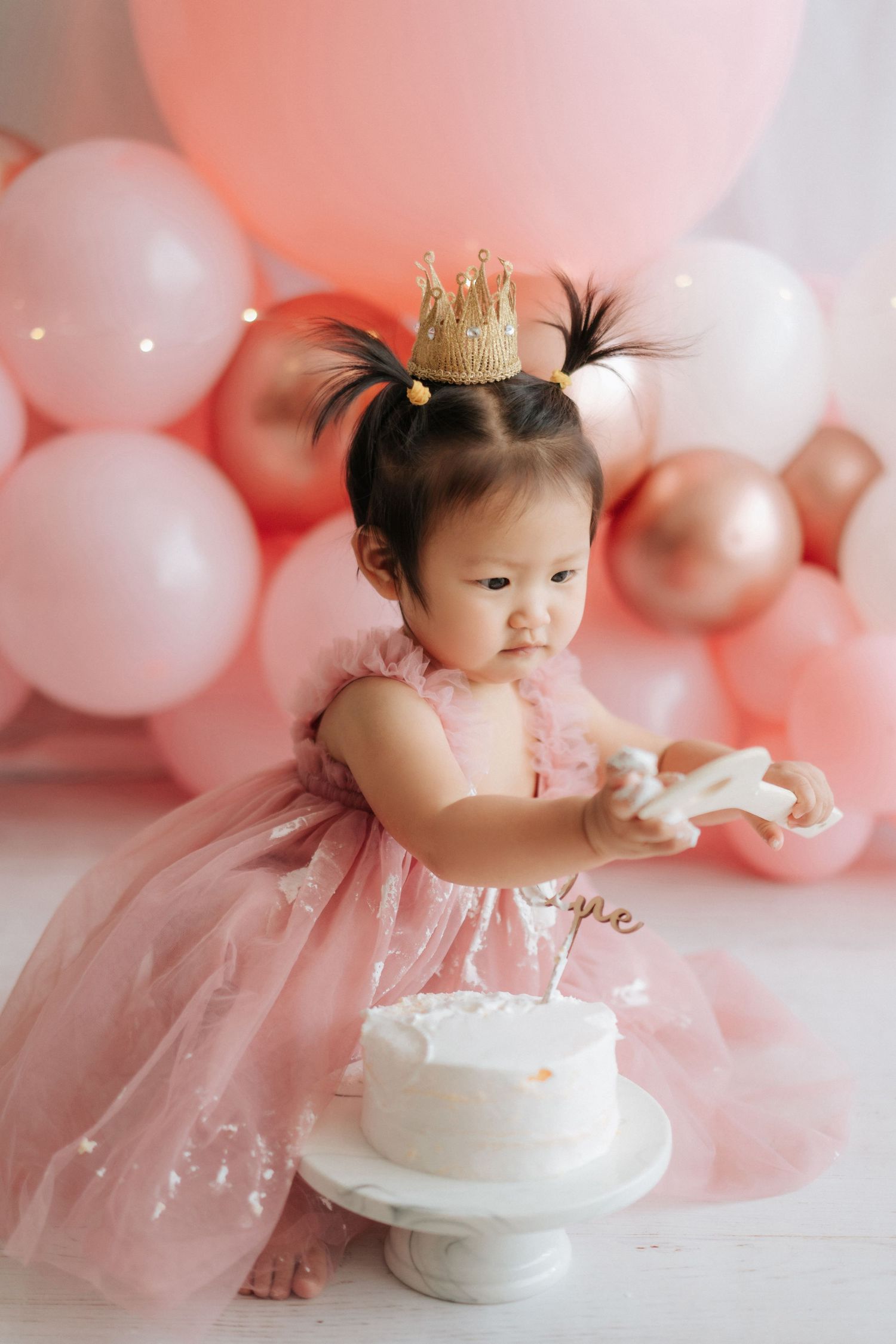 Pink and white balloon decorations create a dreamy backdrop for a first birthday cake smash photo session.