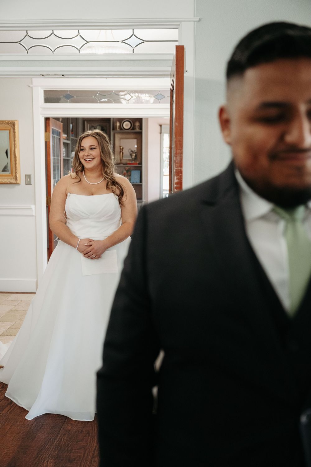 A bride in a white wedding dress shares a first look moment with her groom in a formal indoor setting.