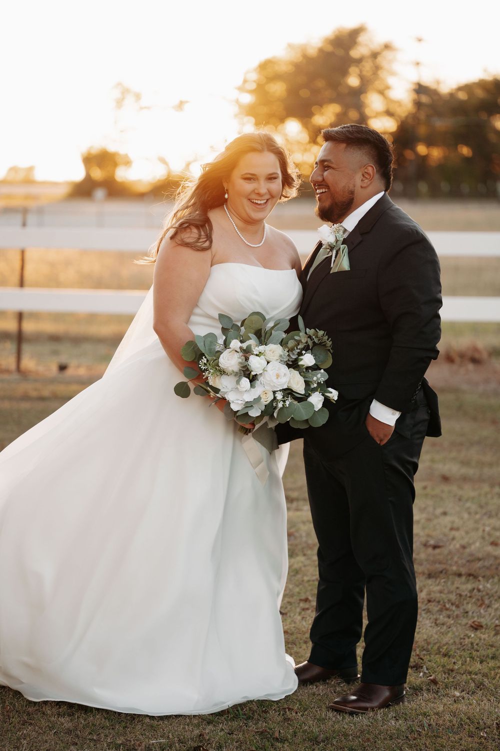 A couple shares a romantic moment at sunset in a field, the bride's white dress flowing in the golden light.