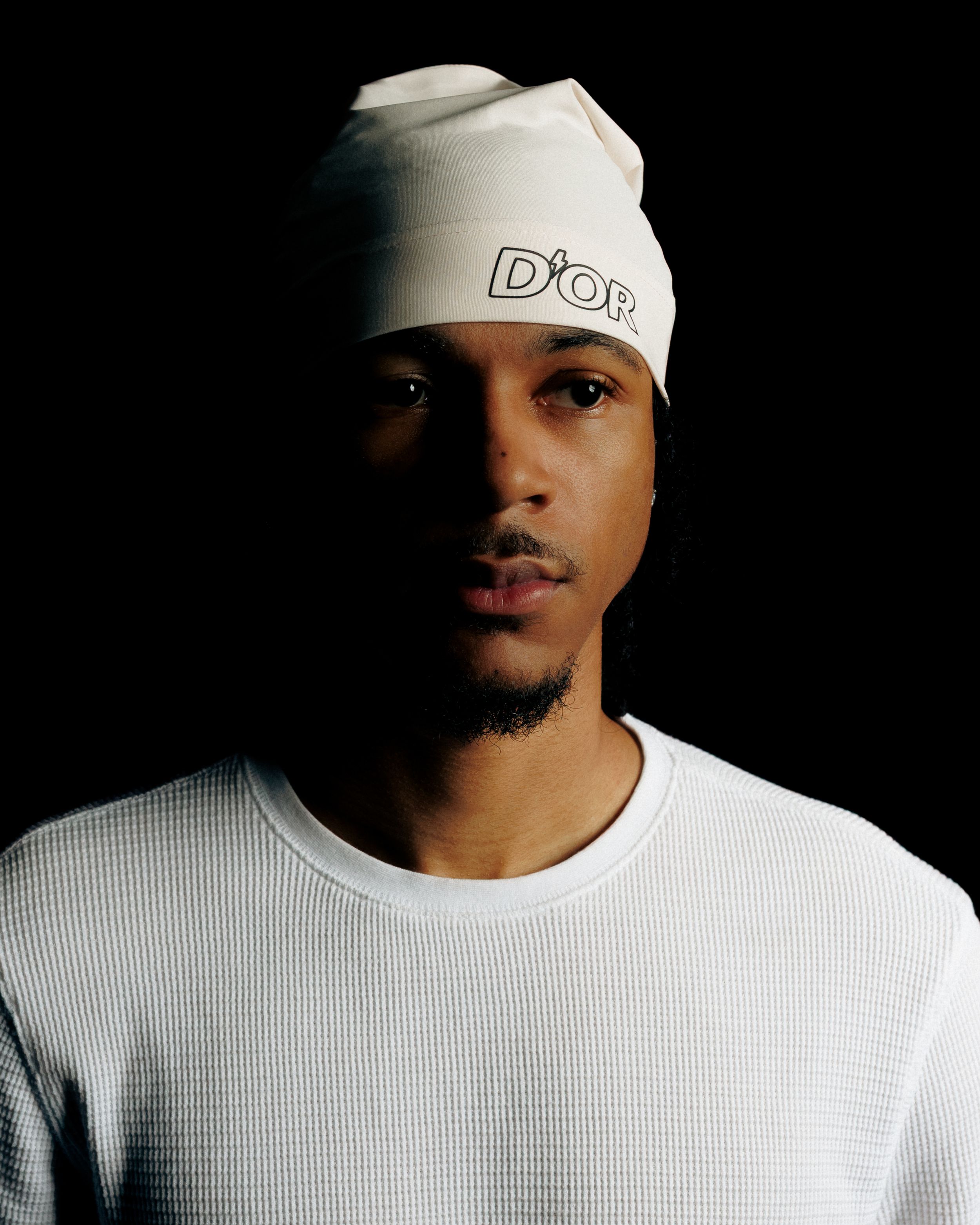 A series of artistic black and white portraits showing a person in a white Dior cap and t-shirt against a dark background.