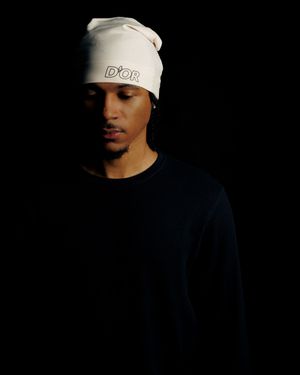 A dramatic low-key portrait against black background featuring someone wearing a white beanie hat.
