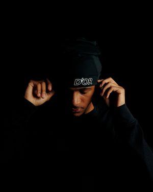 Dramatic dark portrait series showing hands adjusting a black hat against a shadowy background.