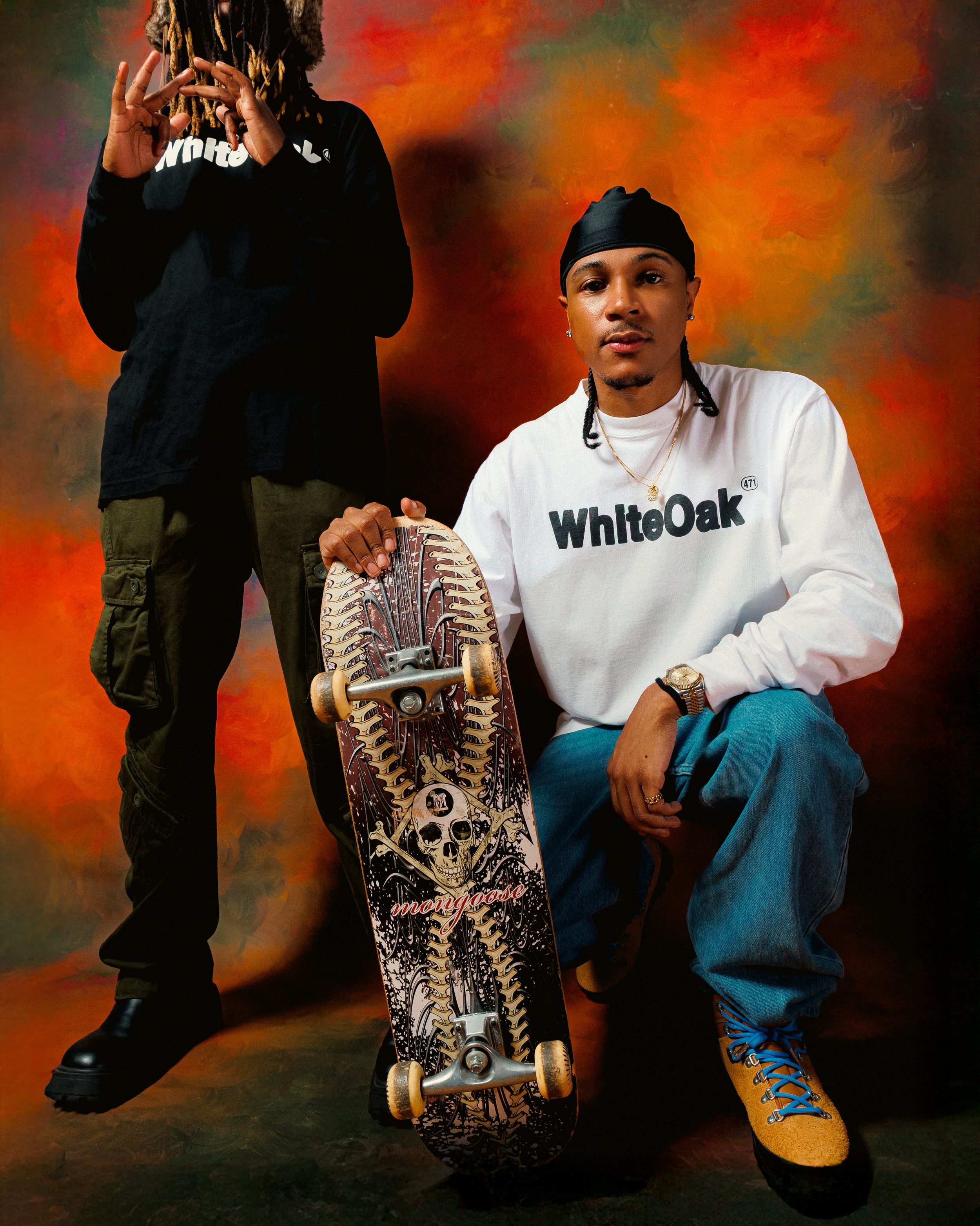 A person wearing a white WhiteOak shirt and jeans sits casually against a dramatic orange and black backdrop.