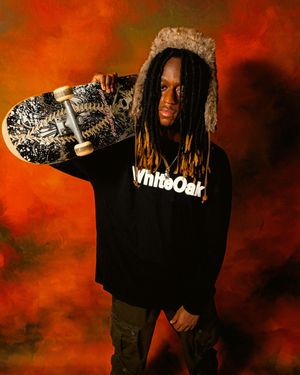 A figure in a black hoodie poses against a dark red and black background with dramatic lighting.