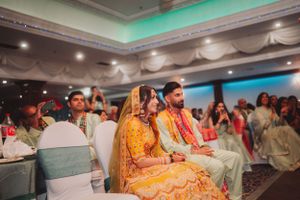 Traditional Indian wedding ceremony with couple seated in ornate yellow and red attire.