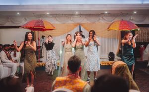 Bridesmaids in vintage-style dresses pose with colorful umbrellas during a wedding reception celebration.