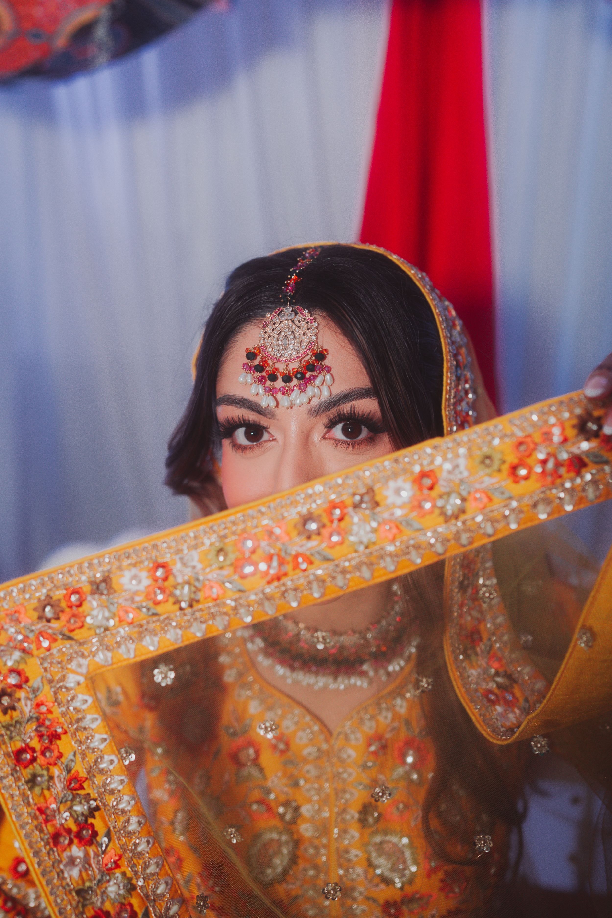 Traditional bridal portrait showing intricate jewelry and embroidered yellow dupatta details.
