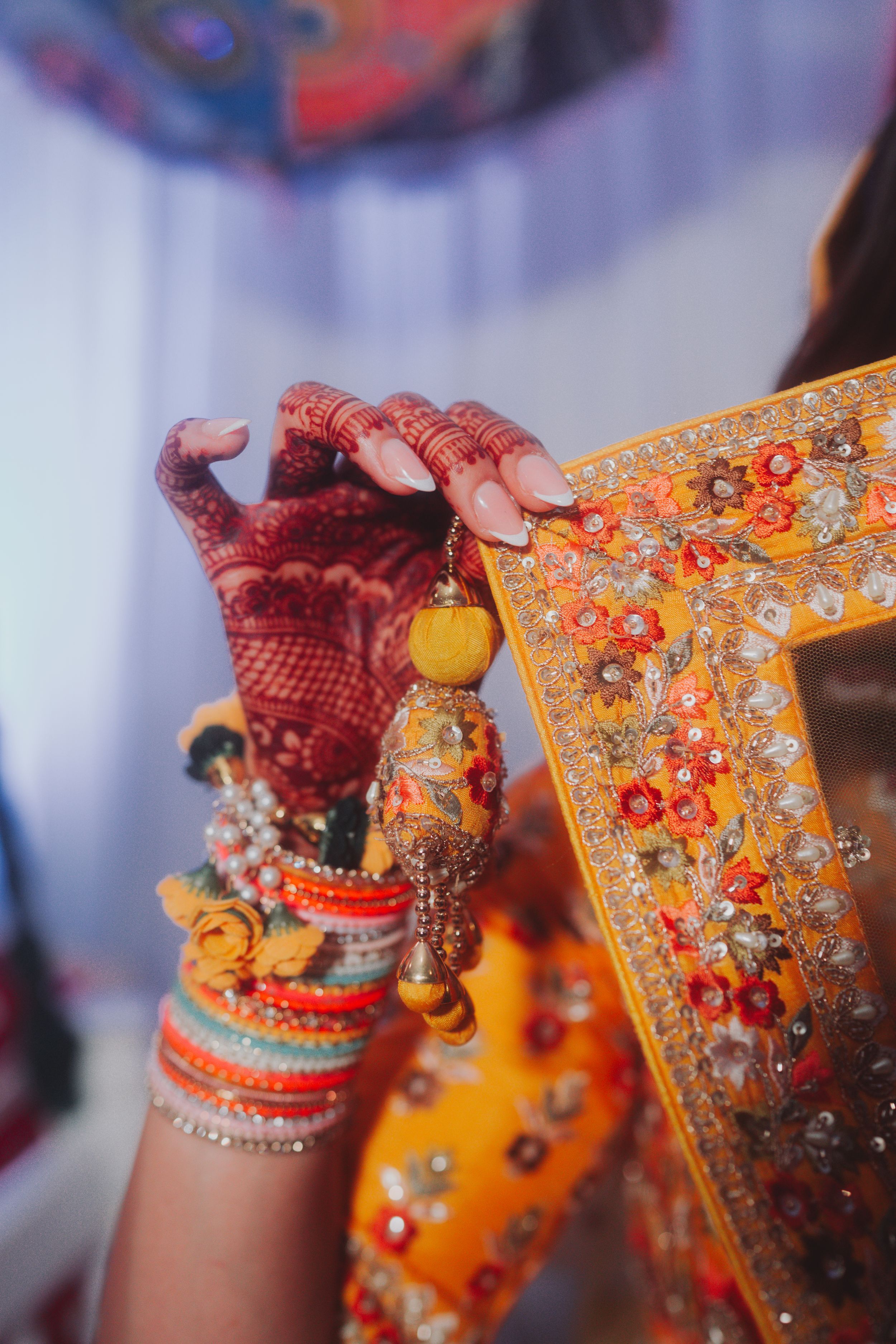 Close-up of hands adorned with henna and bangles holding embroidered fabric with floral details.