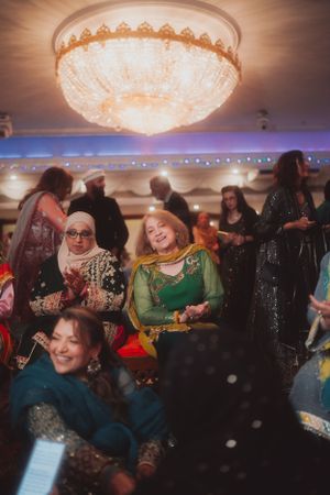 Guests in traditional attire enjoying festivities under an ornate crystal chandelier.