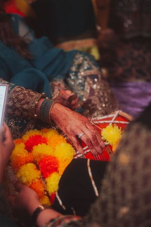 Close-up of mehndi-adorned hands touching colorful marigold flowers during Indian wedding ritual.