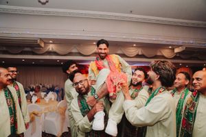 Group of men in traditional green attire lifting someone during wedding celebration.