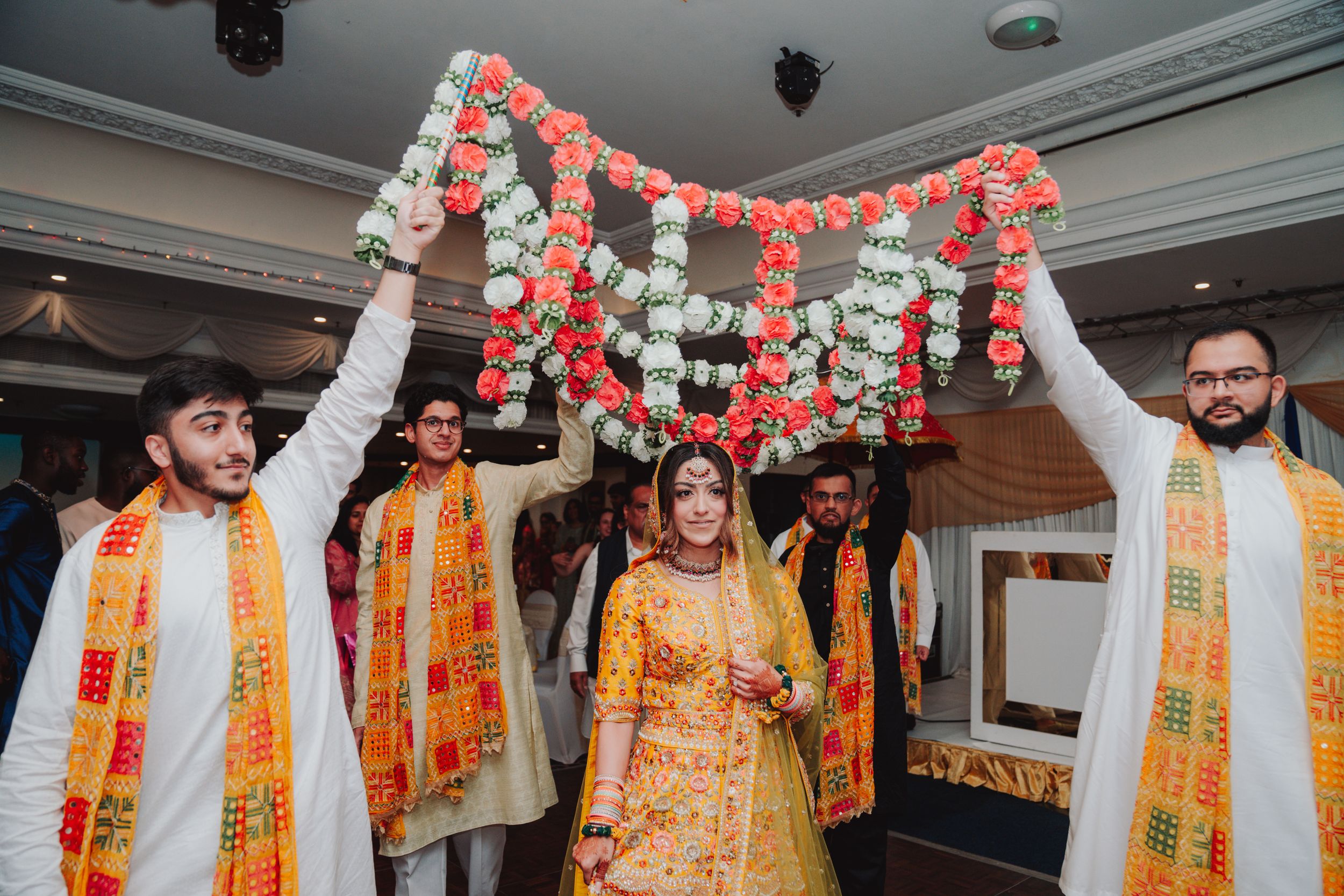 Wedding party holding decorated floral garland during traditional ceremony.