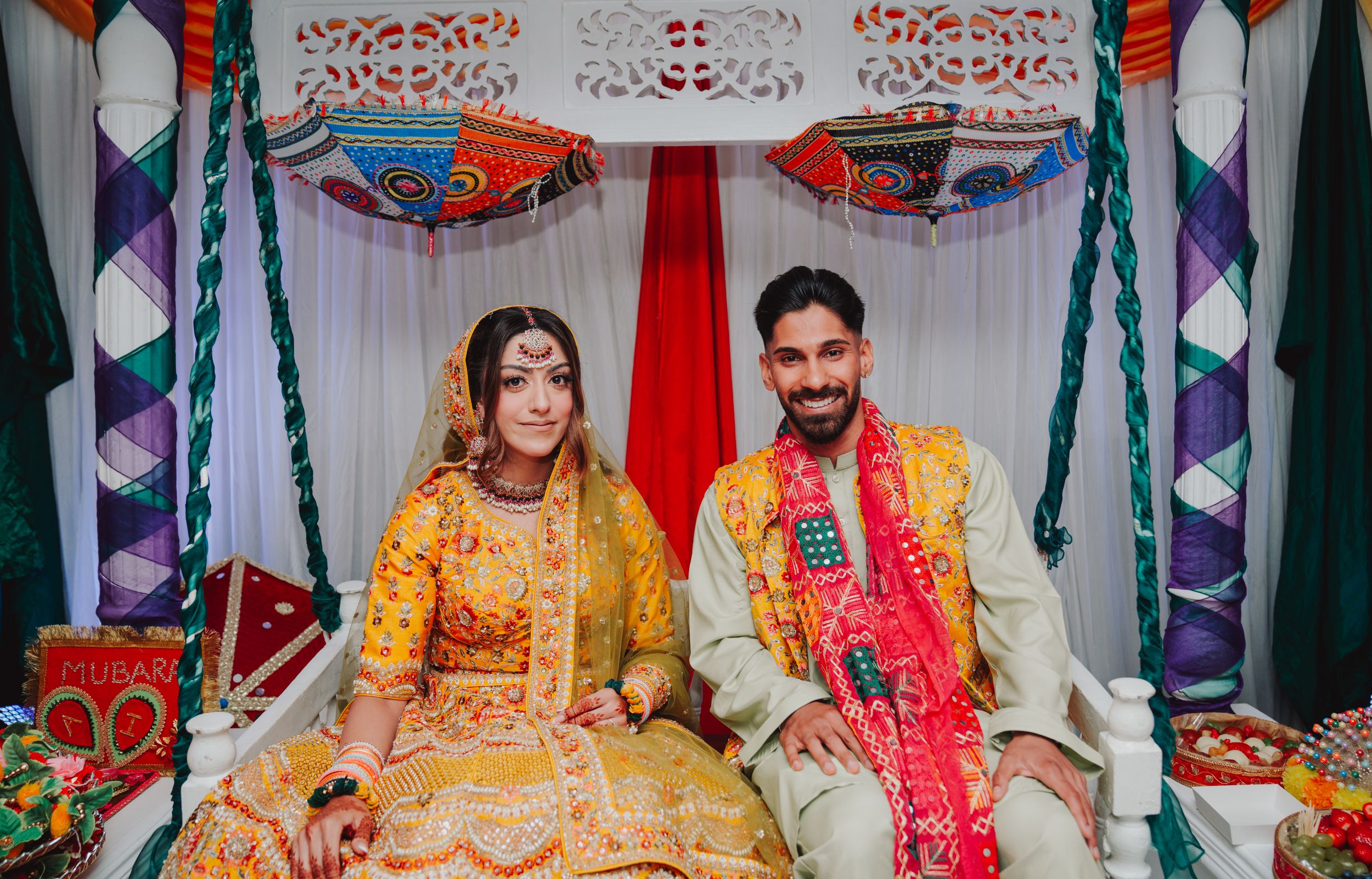 Couple seated on decorated stage in yellow and red traditional Indian wedding attire.