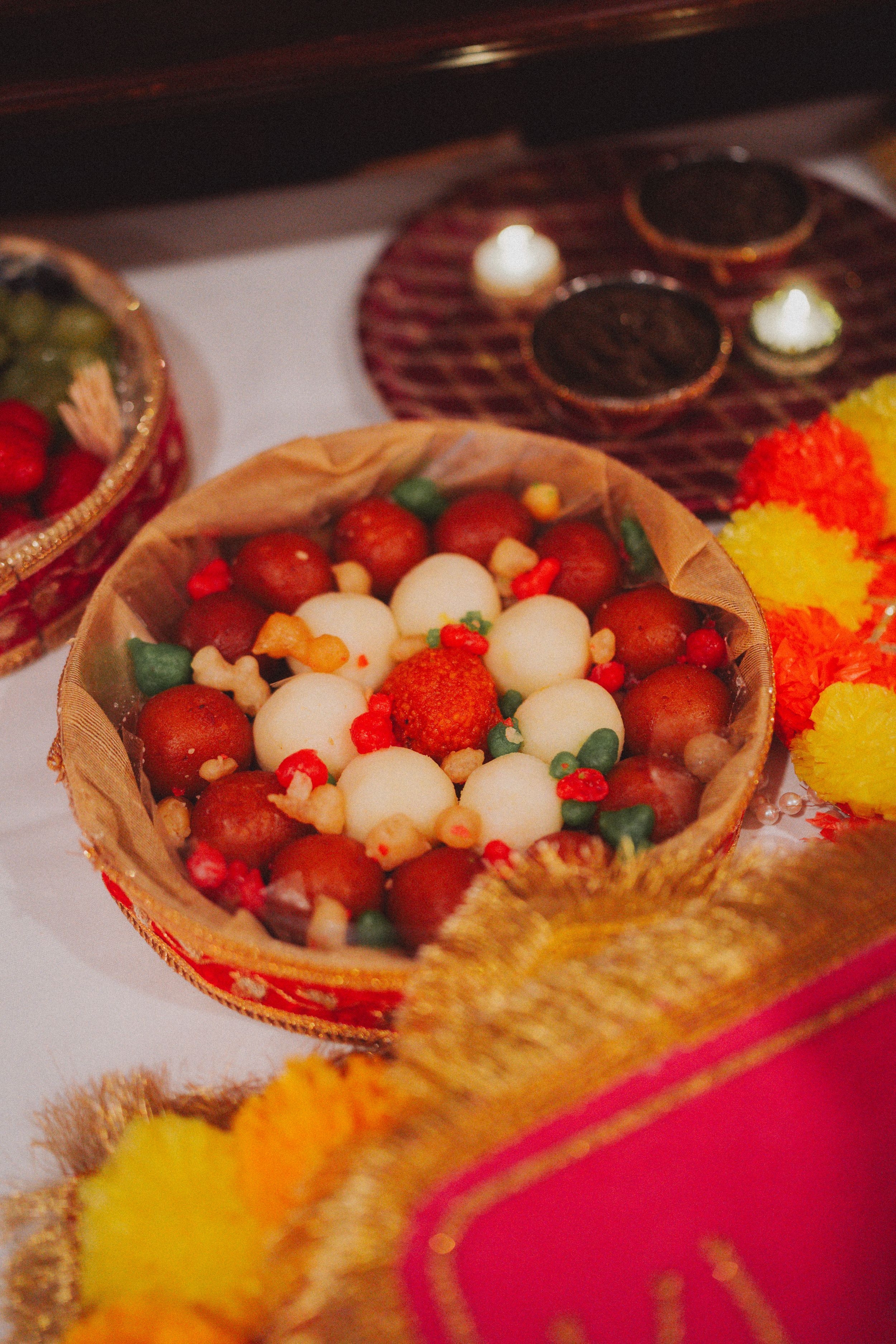 Decorative plate filled with colorful candies and sweets on red fabric at an Indian wedding celebration.