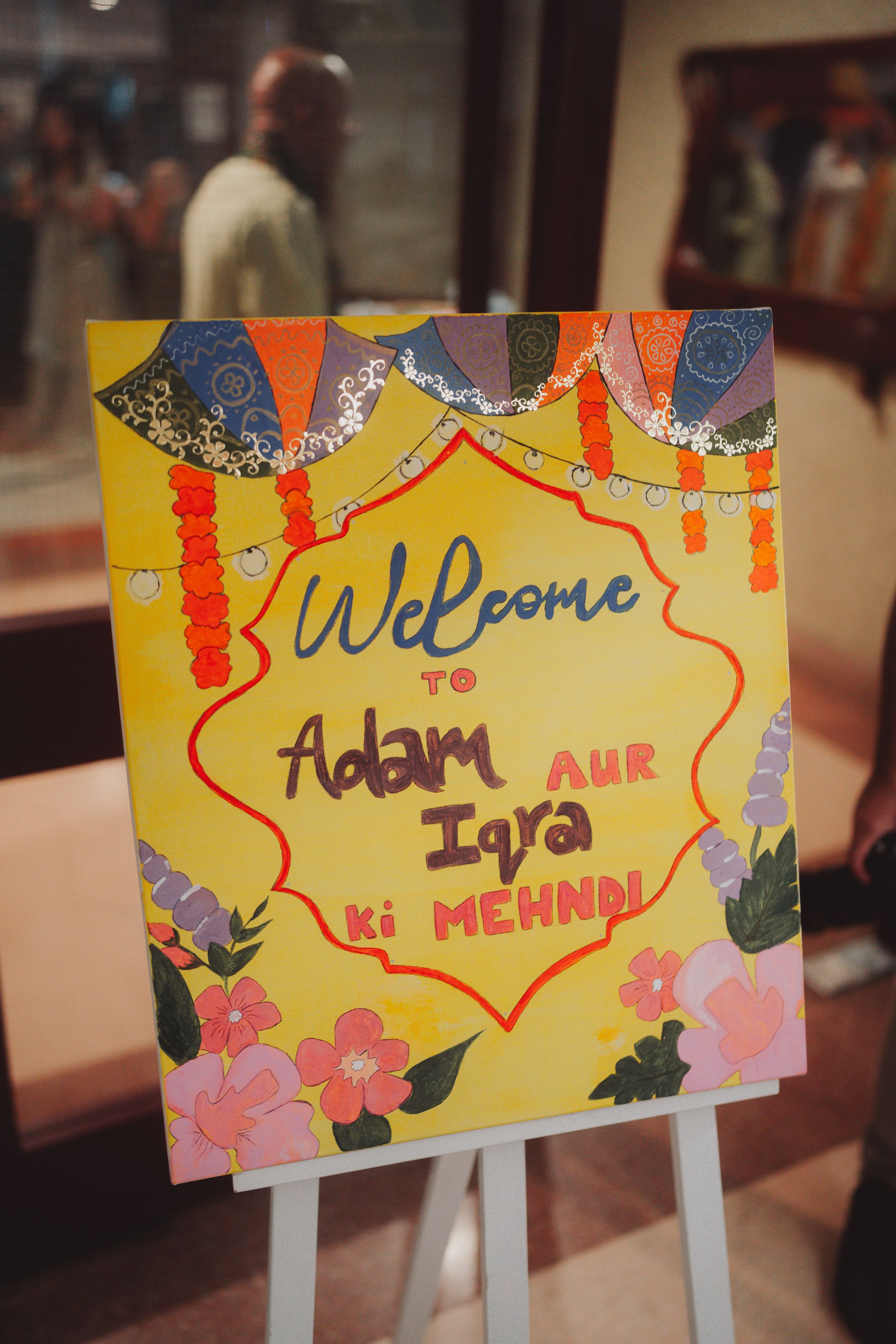 Colorful welcome sign on an easel for a mehndi celebration with floral decorations.