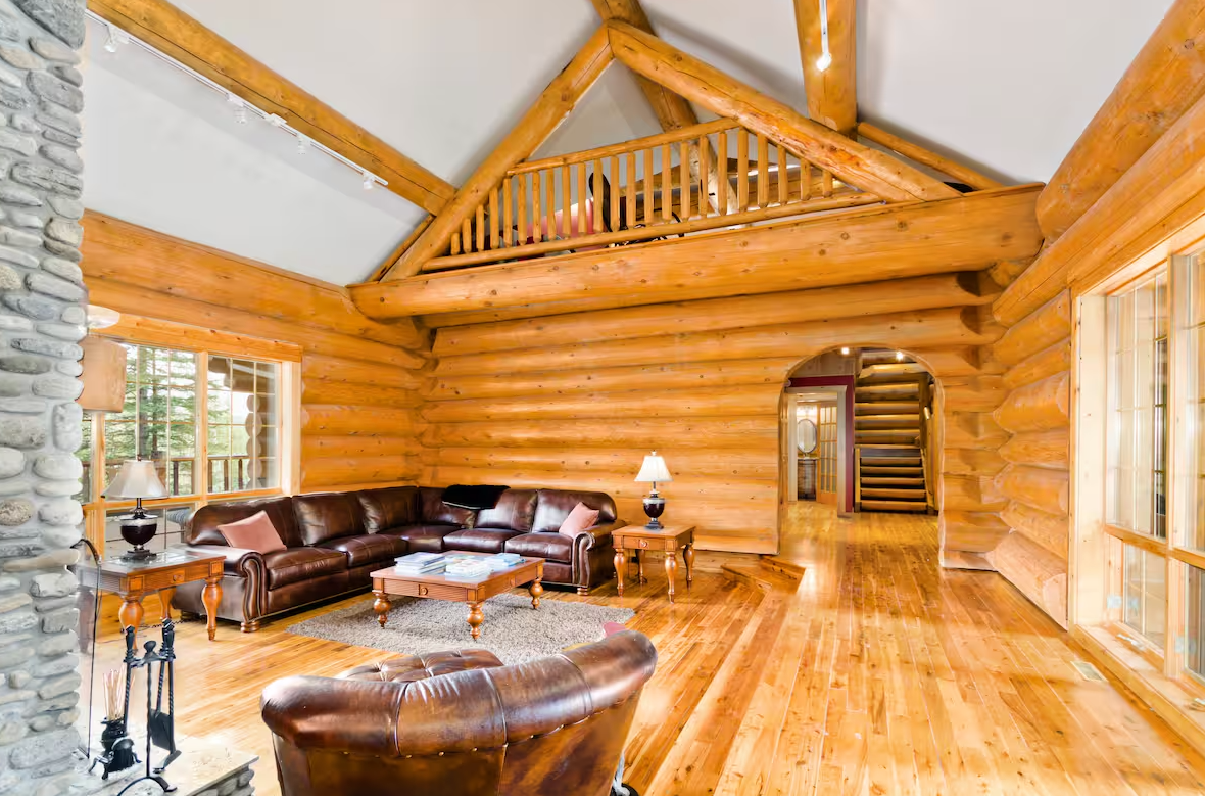 Luxurious log cabin living room with leather furniture and stone fireplace.