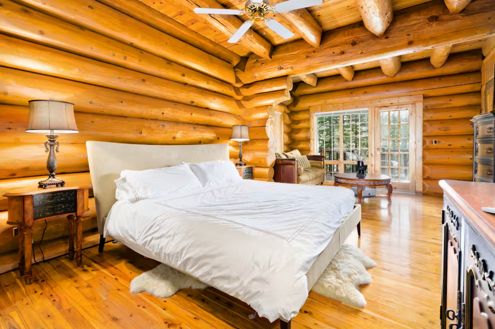 Spacious log cabin bedroom with white bedding and wooden beam ceiling.